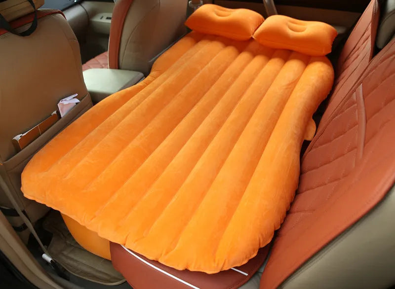 Black inflatable car bed with flocked surface and two pillows, folded next to its storage bag.