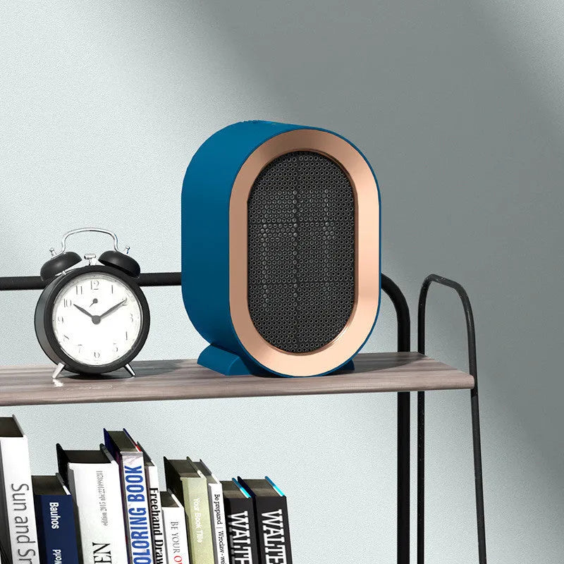 A compact black desktop ceramic fan heater with a mechanical control knob on a wooden desk.