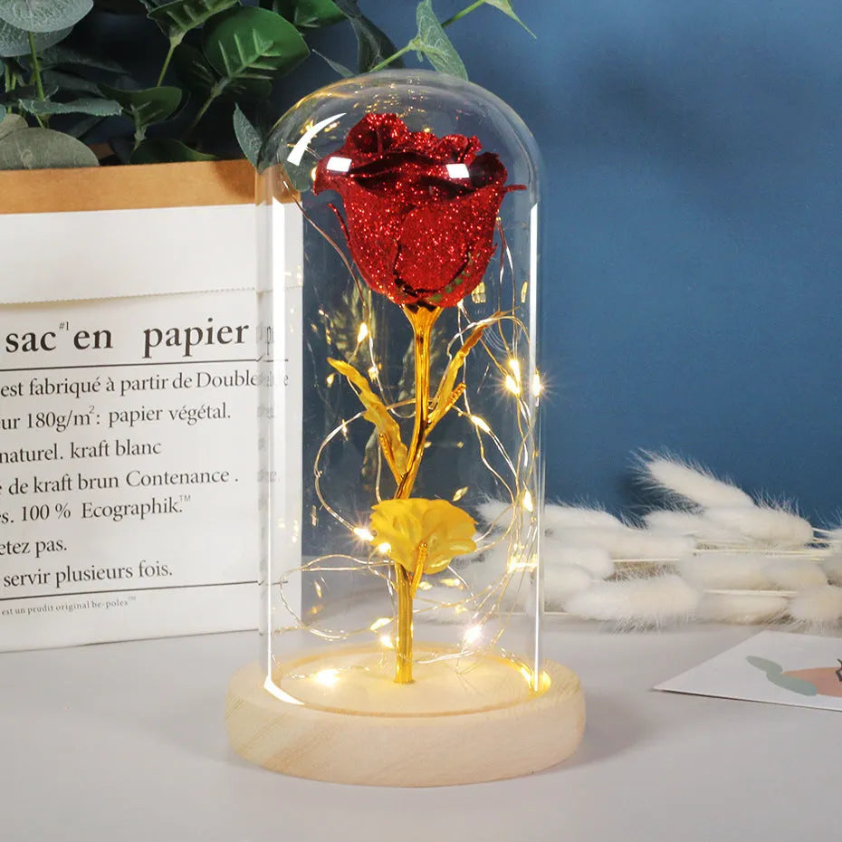 Red eternal rose with warm white LED lights under a glass dome on a table.