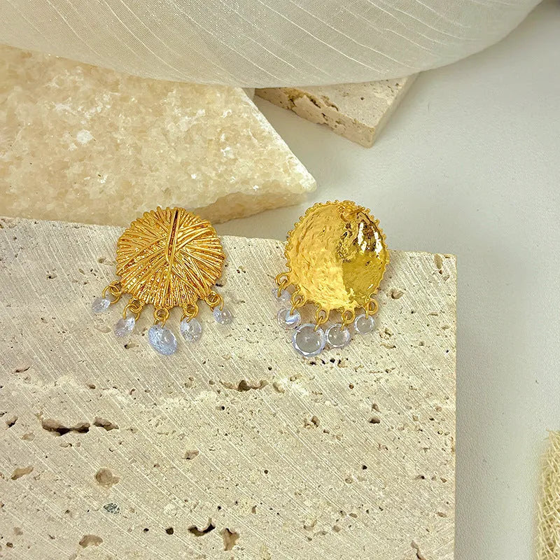 A pair of circular gold geometric hoop earrings on a plain background