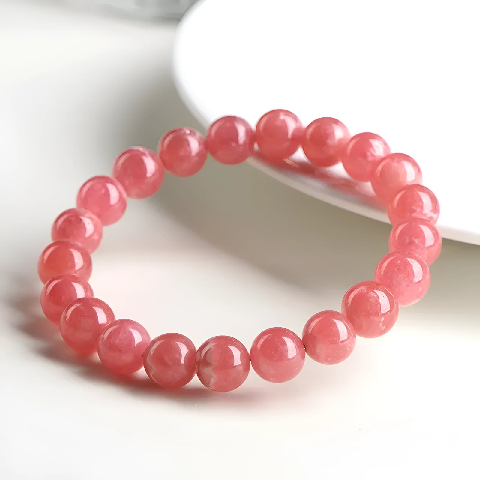 Women's geometric rhodochrosite crystal bracelet with a Longevity Lock centrepiece on a white background.