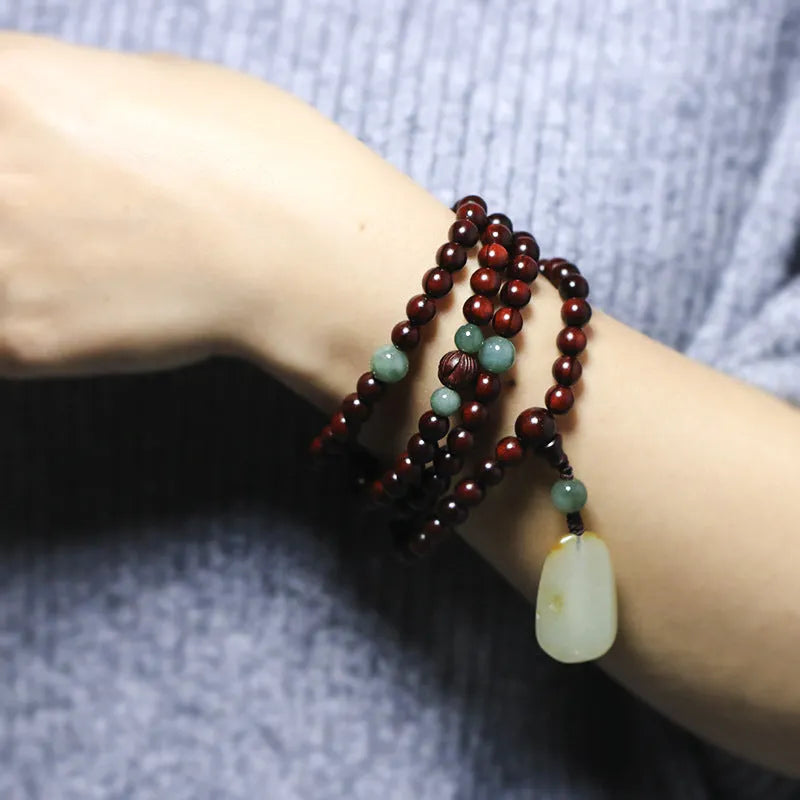 Close-up of a hand-carved rosewood beaded bracelet with 108 6mm beads and a carved Hotian jade pendant.