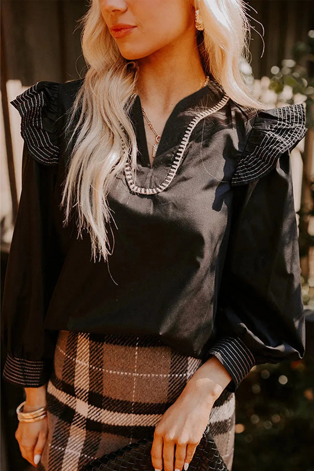 Black women's V-neck blouse with contrast stitching and long ruffle sleeves on a hanger.