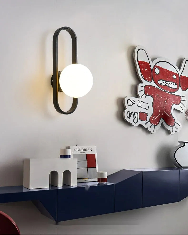 Modern minimalist wall lamp with clear glass shade and black iron mount, showing three light colour settings.