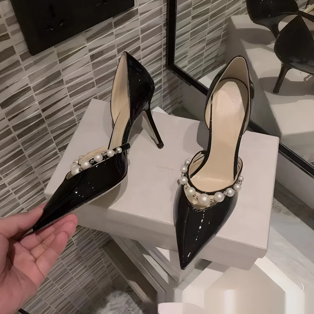 Black pointed toe patent leather women's stiletto heels with pearl decoration on the heel.