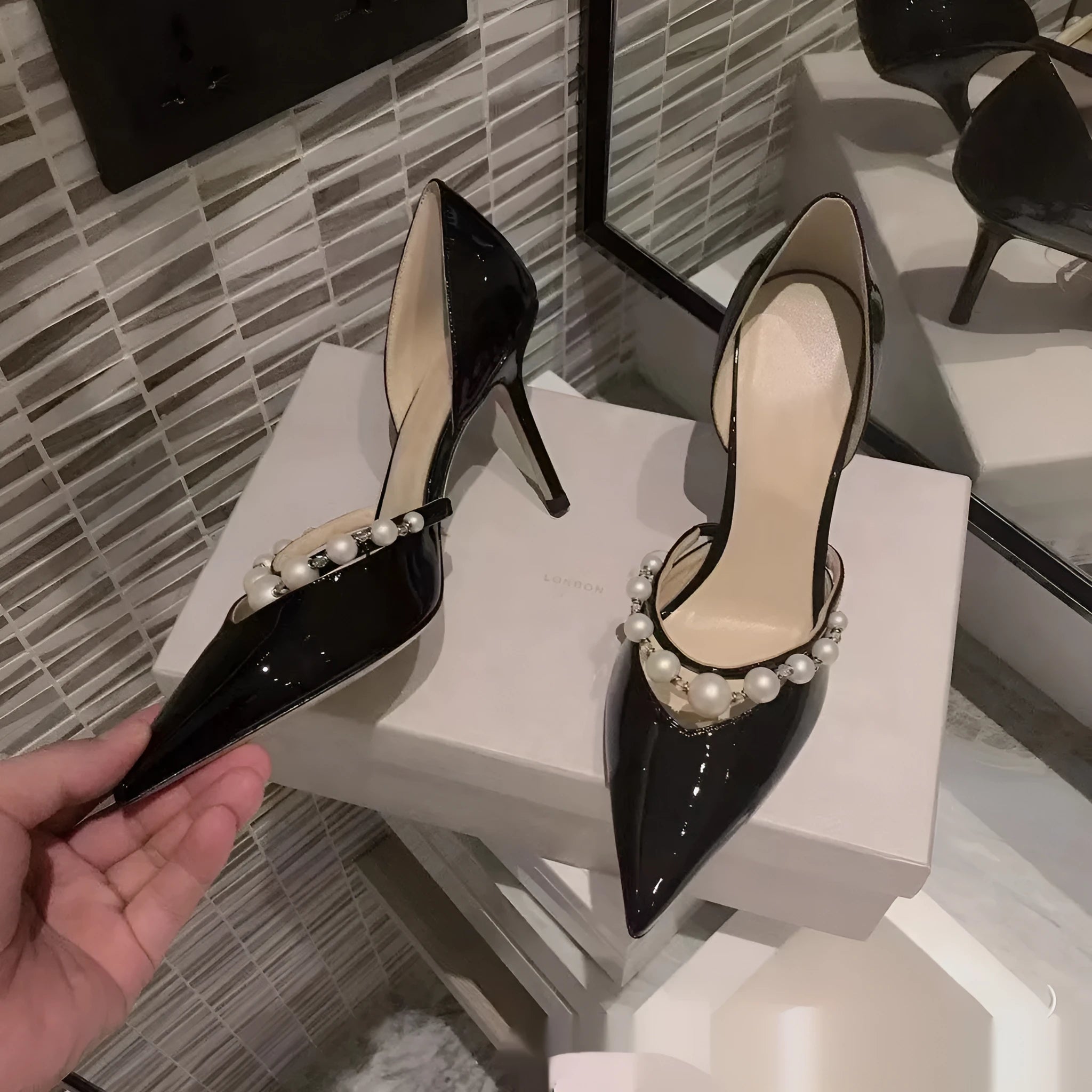 Black pointed toe patent leather women's stiletto heels with pearl decoration on the heel.