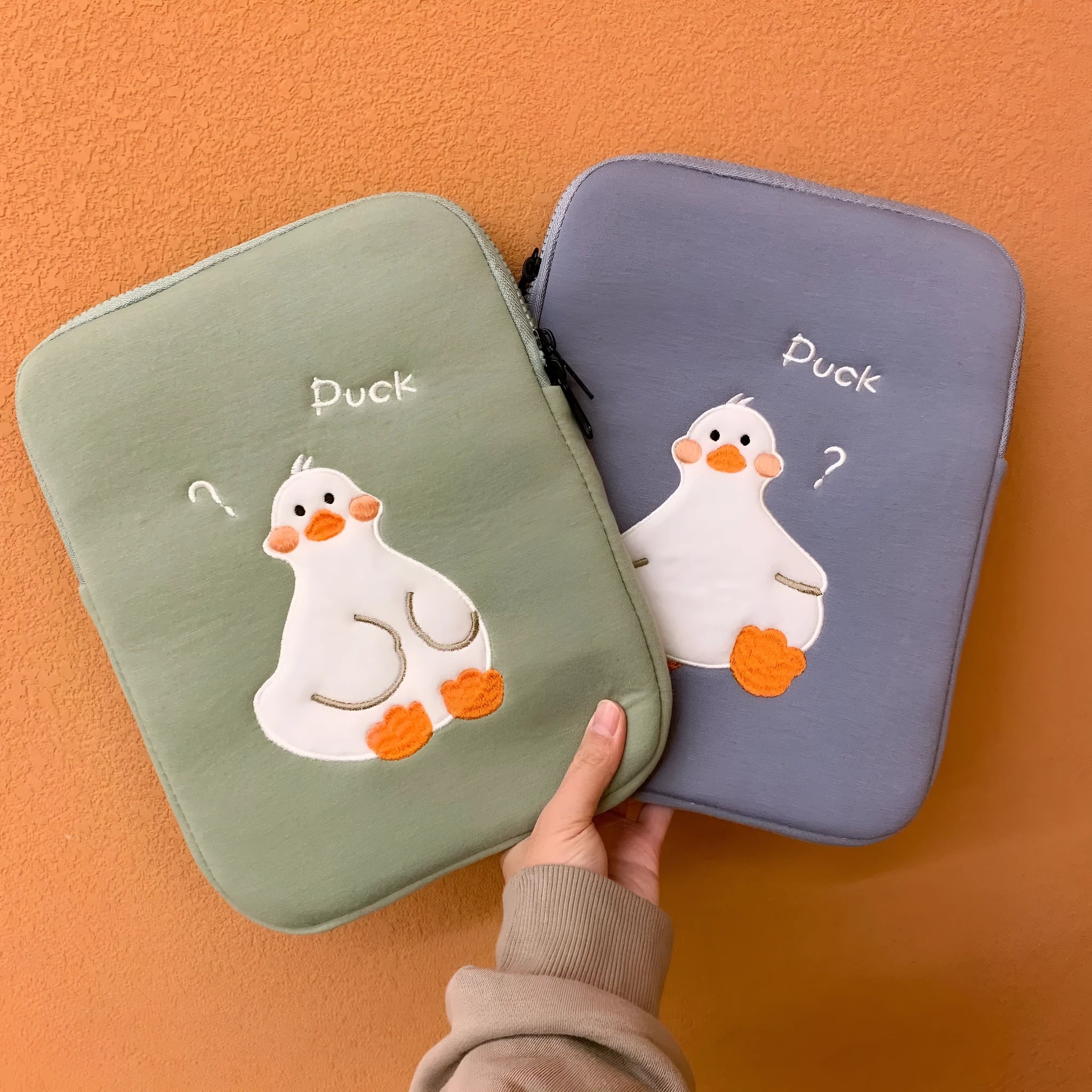Blue tablet case with embroidered cartoon duck design and a silver zipper closure.