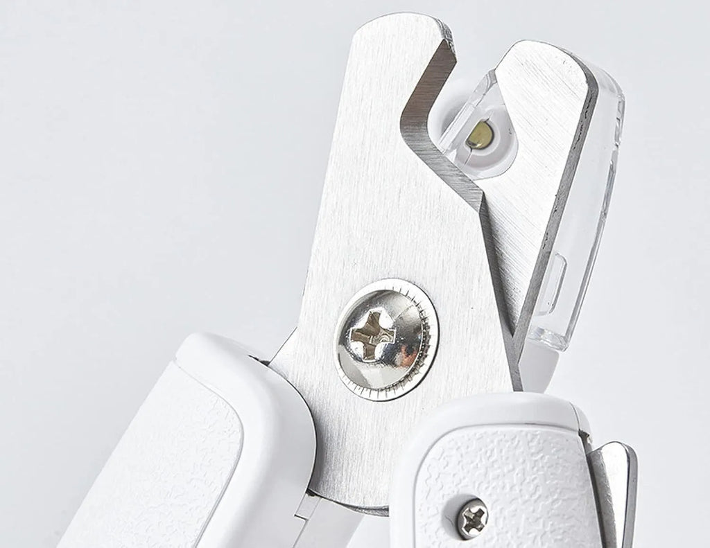 White pet nail clippers with LED light and transparent guard, shown with a separate nail file on a table.