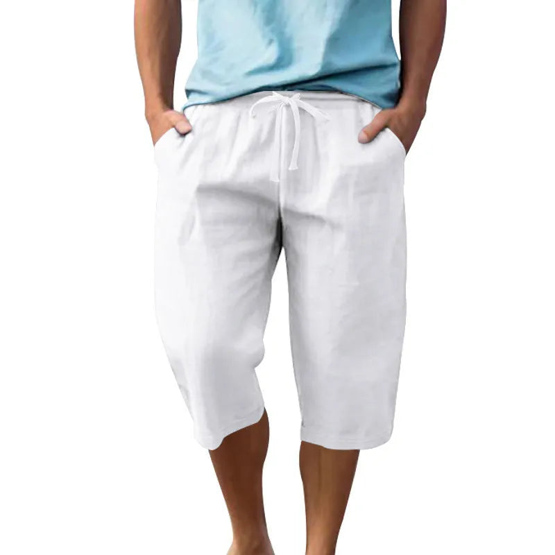 Man wearing loose-fit light khaki linen shorts with a drawstring waist and cropped leg.