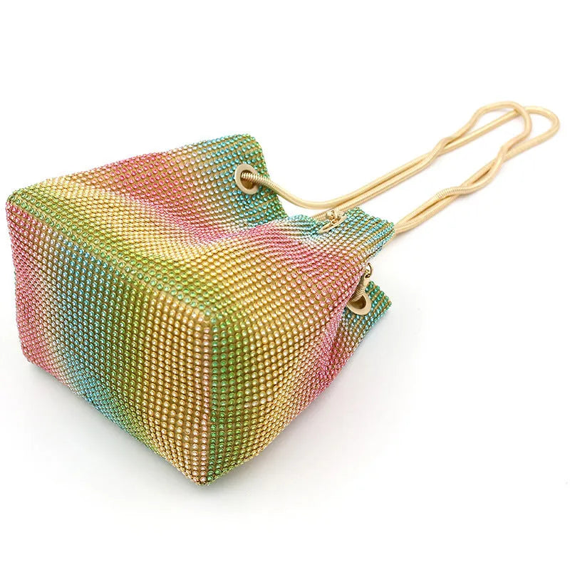 Soft rainbow rhinestone bucket handbag with adjustable strap on a white background.