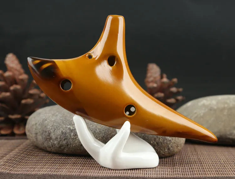 Yellow 12-hole ceramic Alto C ocarina with smoldering finish and lanyard on a surface