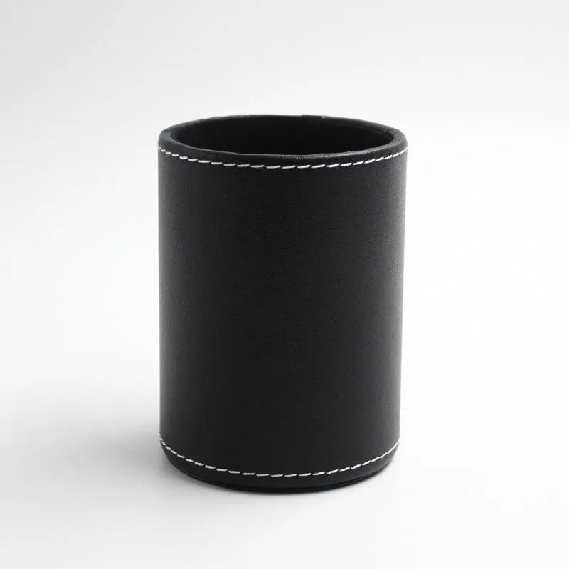 Round black leather pen container on a desk holding pens and pencils.