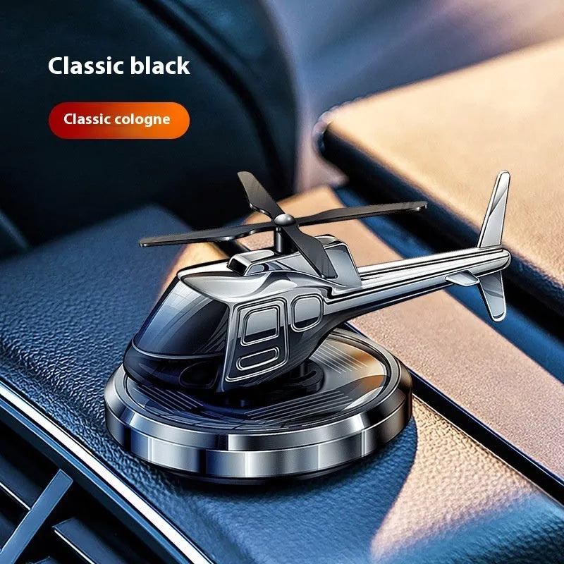 Silver metal solar-powered helicopter car air freshener with spinning blades on a dashboard.
