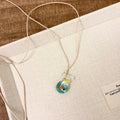 Women's coloured glaze pendant necklace on a braided cotton and linen clavicle chain, showing artisan finish.