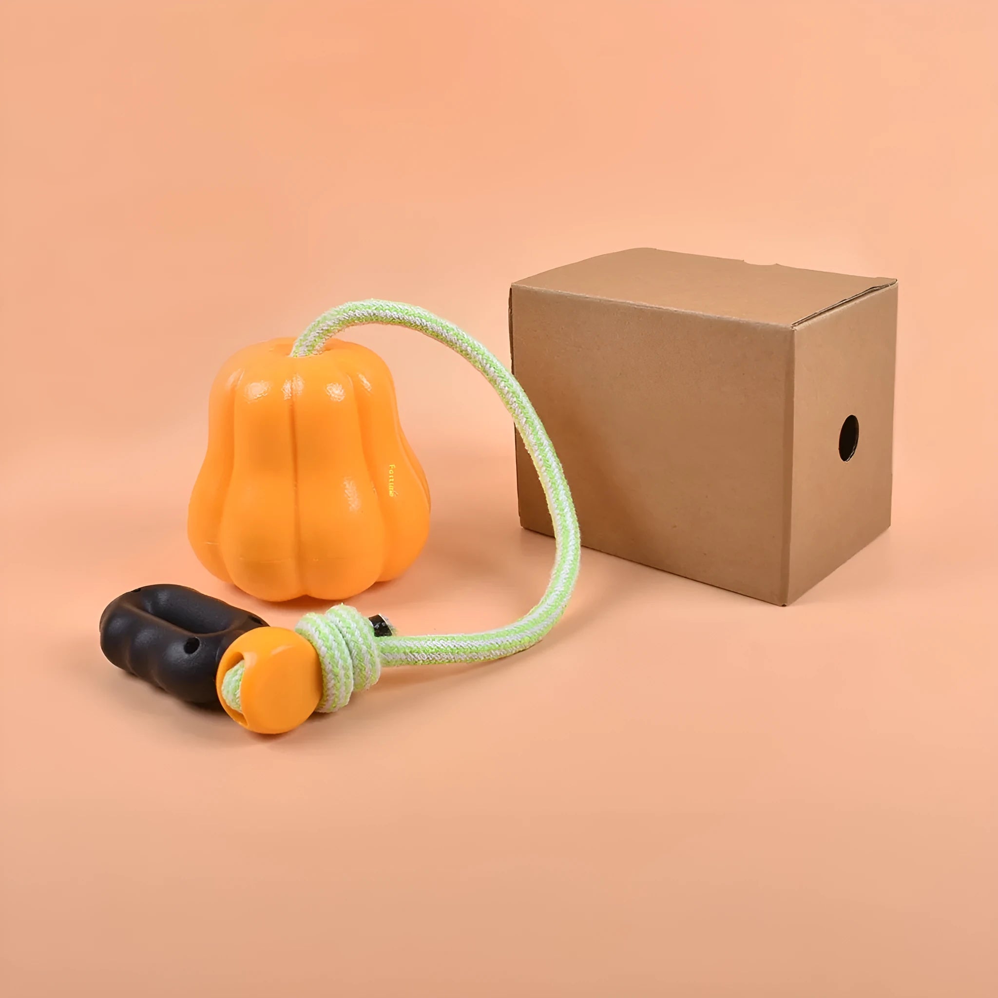 Orange plastic molar-shaped dog chew toy with rope, placed on grass for outdoor use.