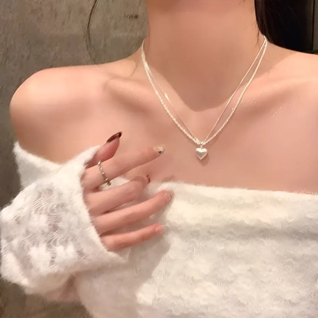 Double-layer brushed silver heart pendant necklace on a model, showing adjustable chain length.