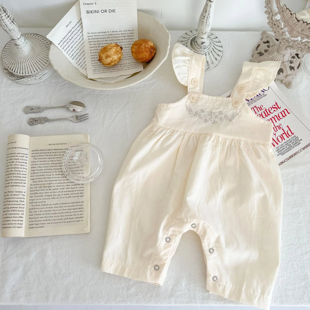 Baby girl wearing a loose-fit cotton suspender romper with adjustable straps in an apricot colour.