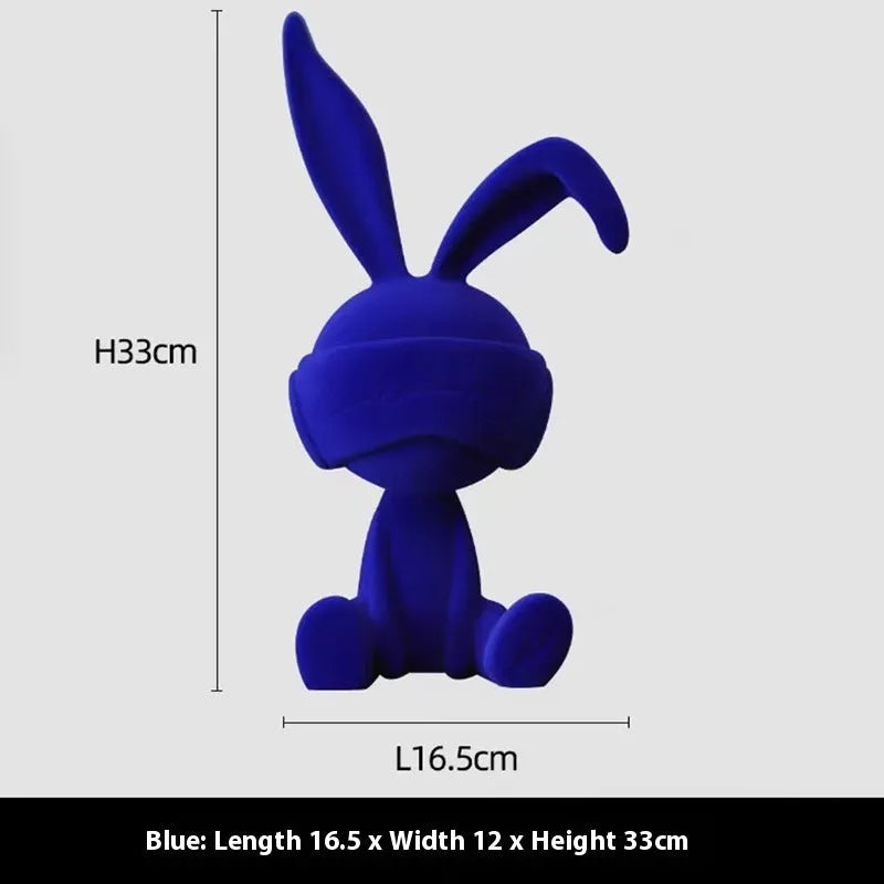 Suede blindfold rabbit resin ornament in blue, green, or red colour on a table.