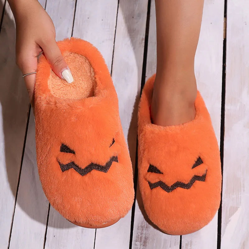 Orange Halloween pumpkin-themed plush indoor slippers with a non-slip sole on a wooden floor.
