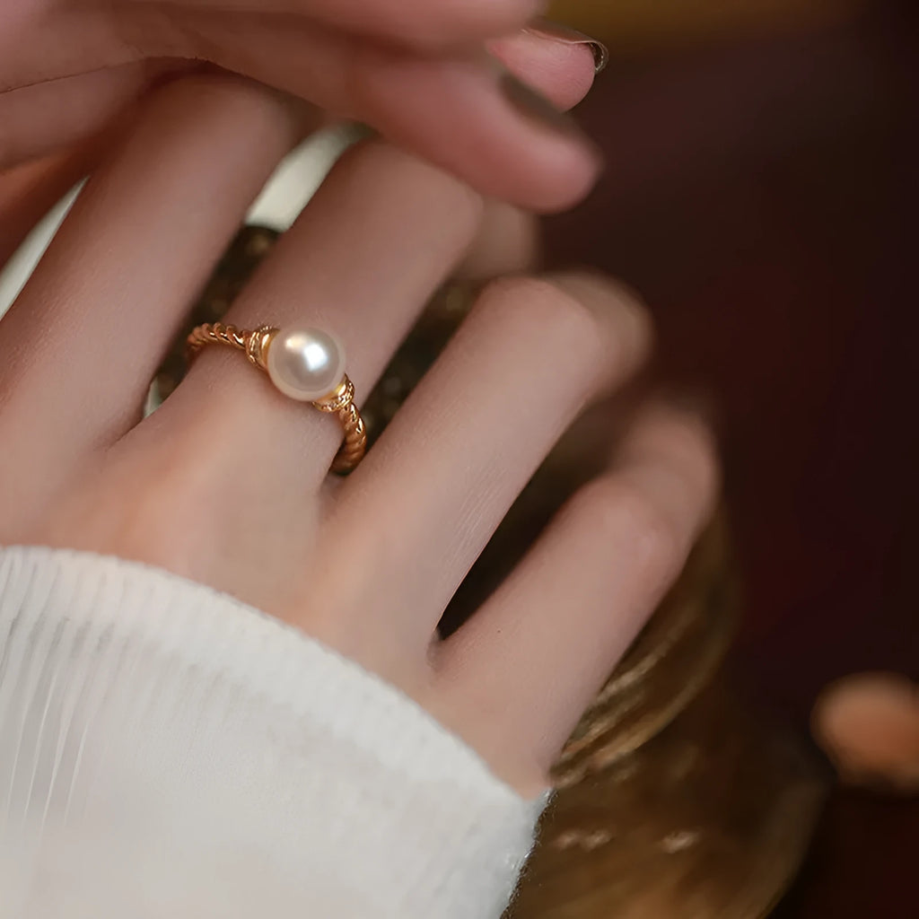 Close-up of an adjustable geometric twist ring in copper with a central pearl inlay, shown on a finger.