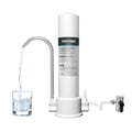 White countertop carbon rod water purifier connected to a household kitchen faucet with replaceable filter element.
