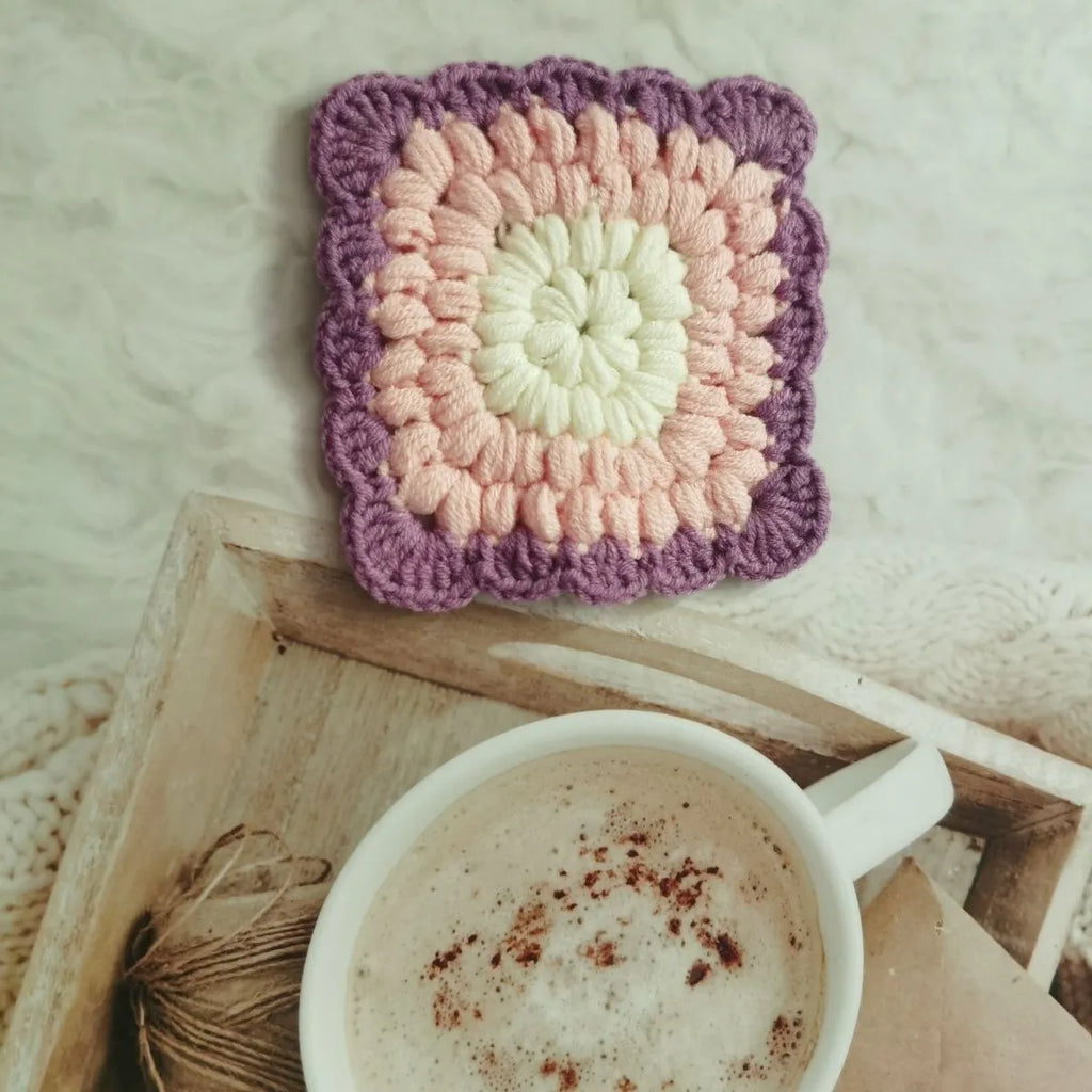 Hand-crocheted wool coaster with lattice pattern in Dream Purple colour on a wooden table.