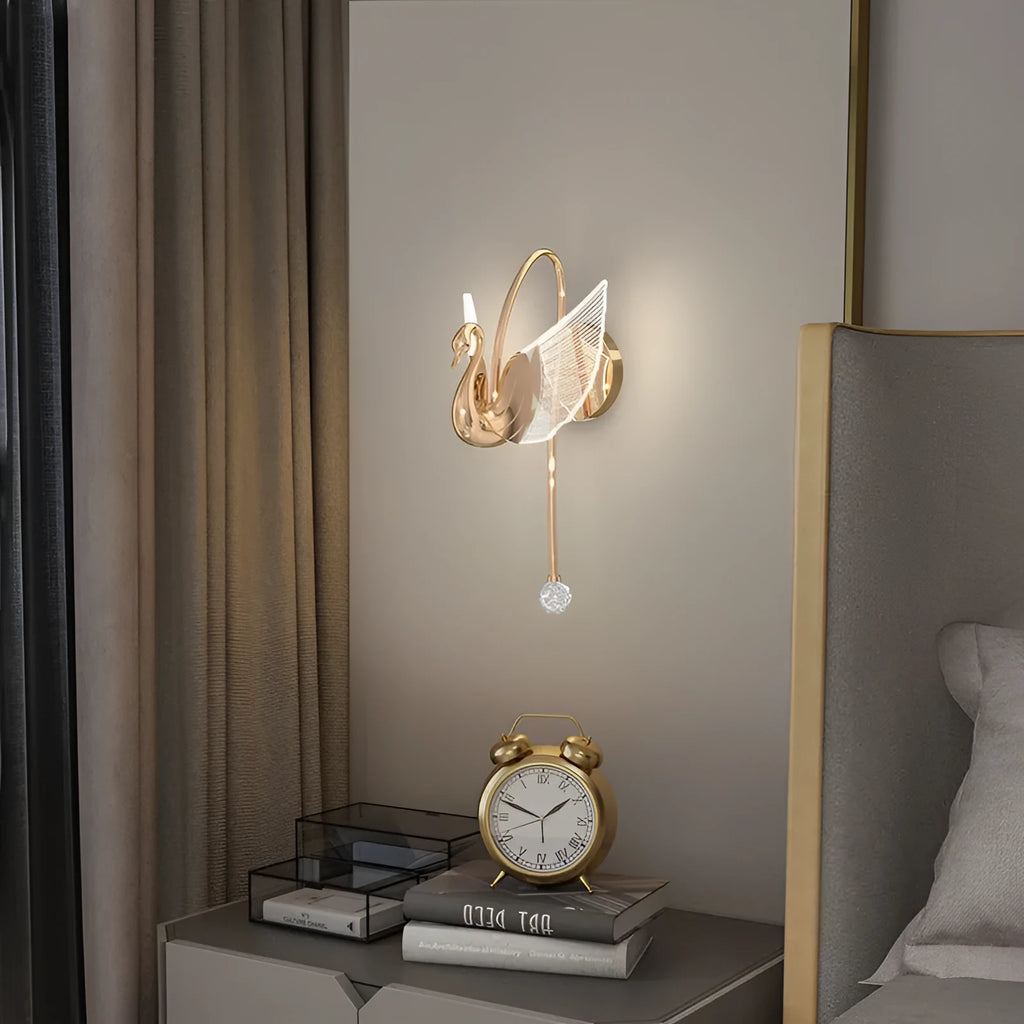 Gold modern swan-shaped wall lamp with acrylic shade mounted beside a bed.