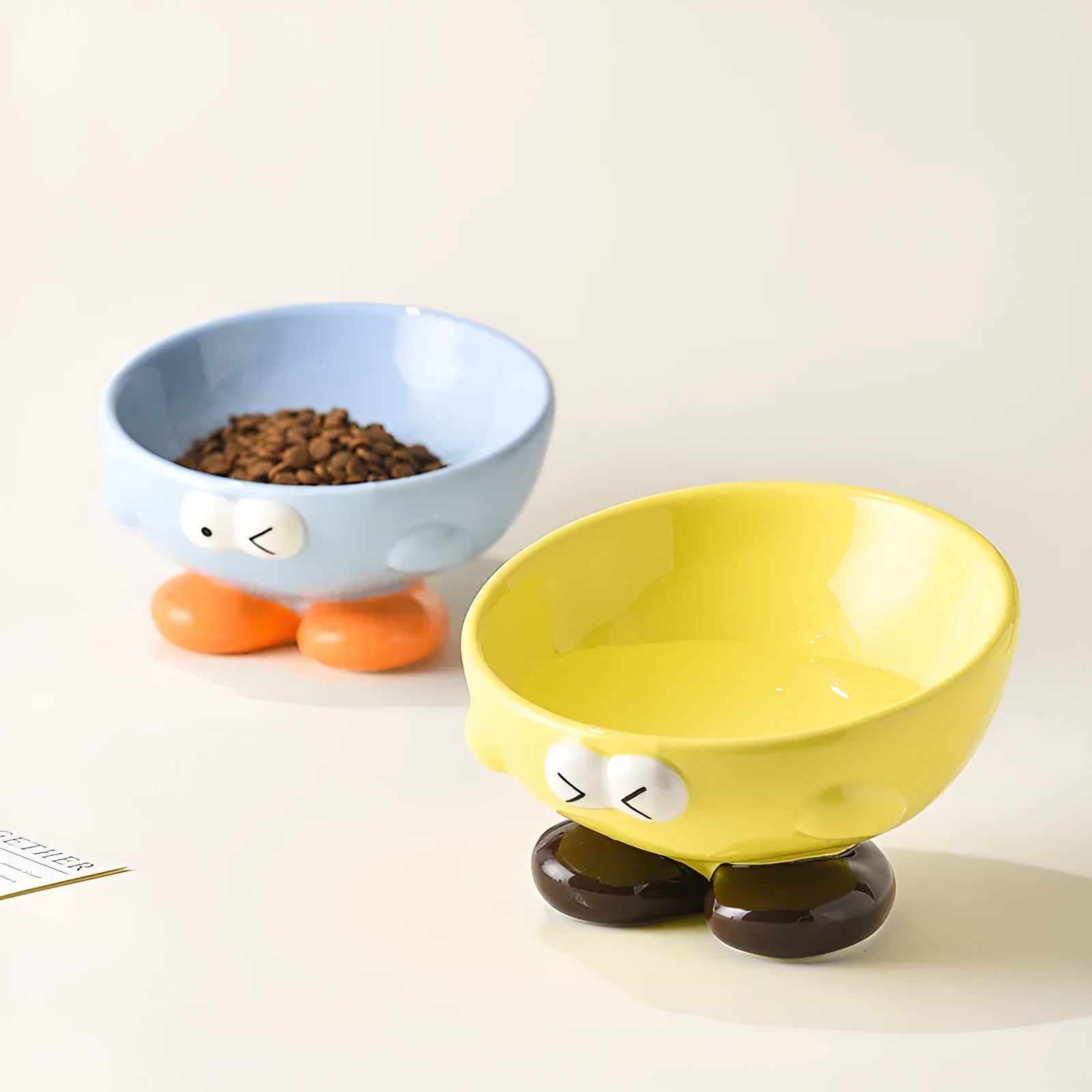 Ceramic slanted pet bowl with cute expression design in blue, yellow, and set colours for cervical spine support.