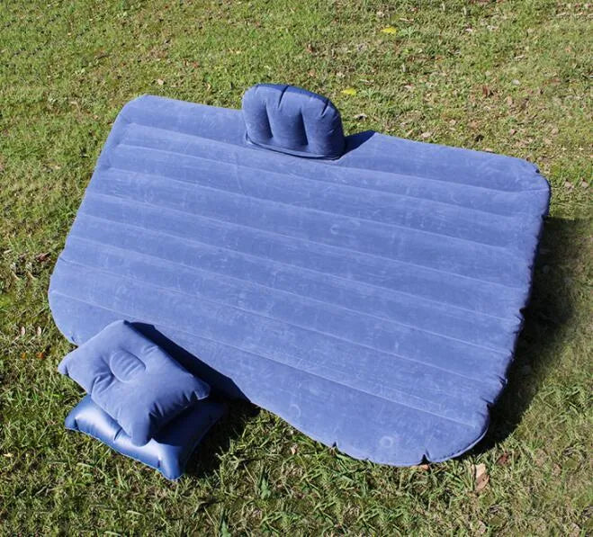 Black inflatable car bed with flocked surface and two pillows, folded next to its storage bag.