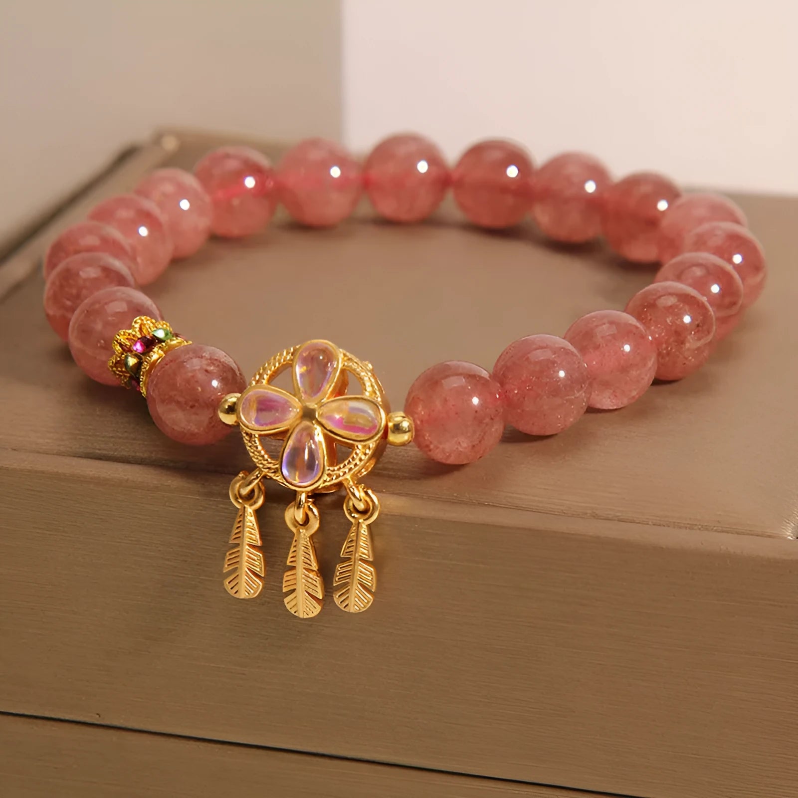 Women's strawberry quartz dream catcher ball pendant bracelet on wrist.