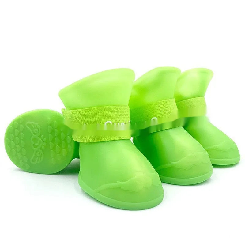 Set of four soft-soled rubber rain shoes for dogs in various colours on a wet surface.