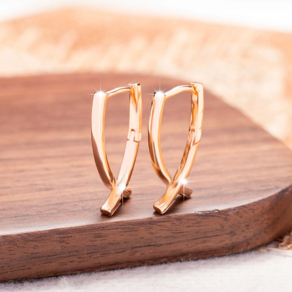 Rose gold tone cross-shaped copper earrings on a flat surface, showing polished finish and push-back clasp.