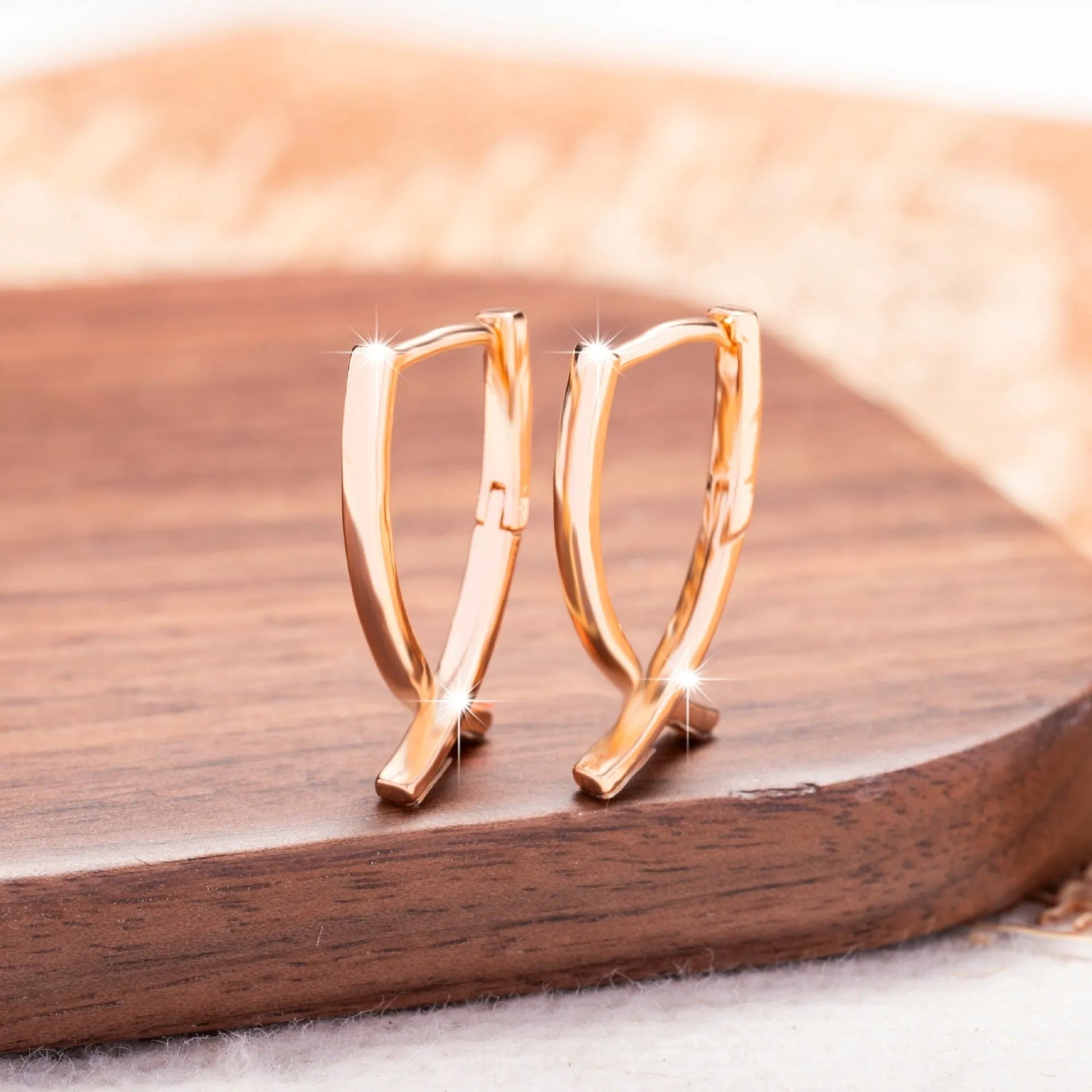 Rose gold tone cross-shaped copper earrings on a flat surface, showing polished finish and push-back clasp.