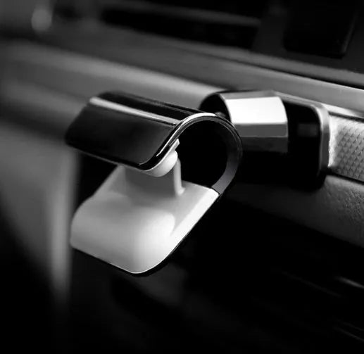 Black universal car phone holder with 360-degree rotating head and adhesive mount on a car dashboard.