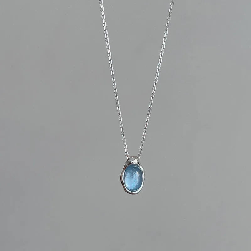 Close-up of a navy blue geometric water drop pendant on an adjustable silver-tone cross chain necklace.