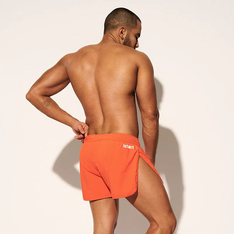 Man wearing orange micro-elastic polyester beach shorts for surfing or swimming.