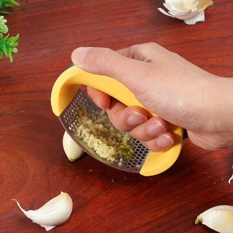 Stainless steel garlic press with coloured ergonomic handle on a kitchen counter.