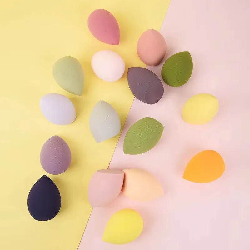 Set of seven coloured makeup sponges in different shapes on a pink background
