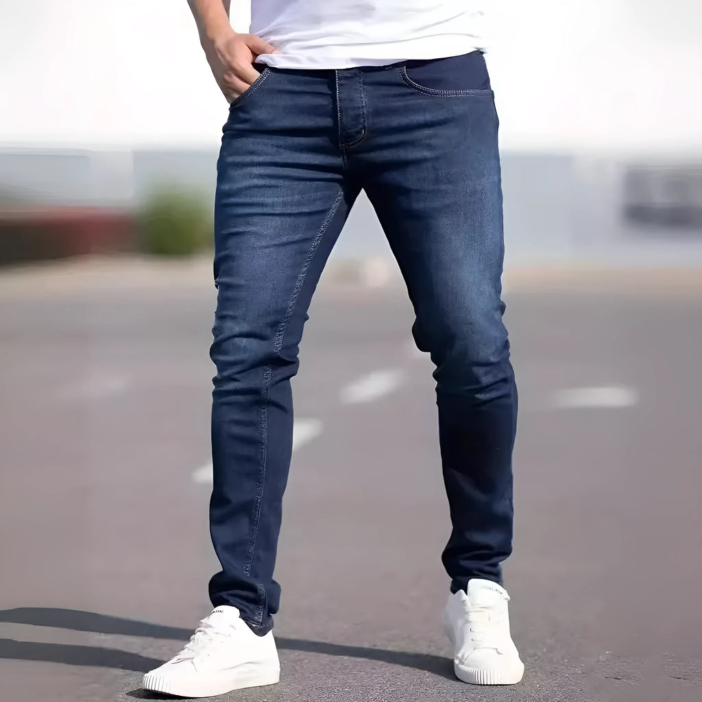 Men's dark blue skinny-fit cotton jeans with a mid-rise waist and zipper fly on a plain background.