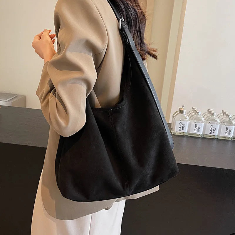 Women's suede bucket bag in black with stitching detail, single shoulder strap, and outer sandwich pocket