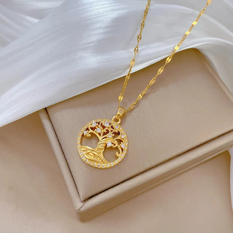 Close-up of a gold necklace with an ornate tree pendant featuring sparkling crystals and a white mother-of-pearl centre, on an adjustable chain.