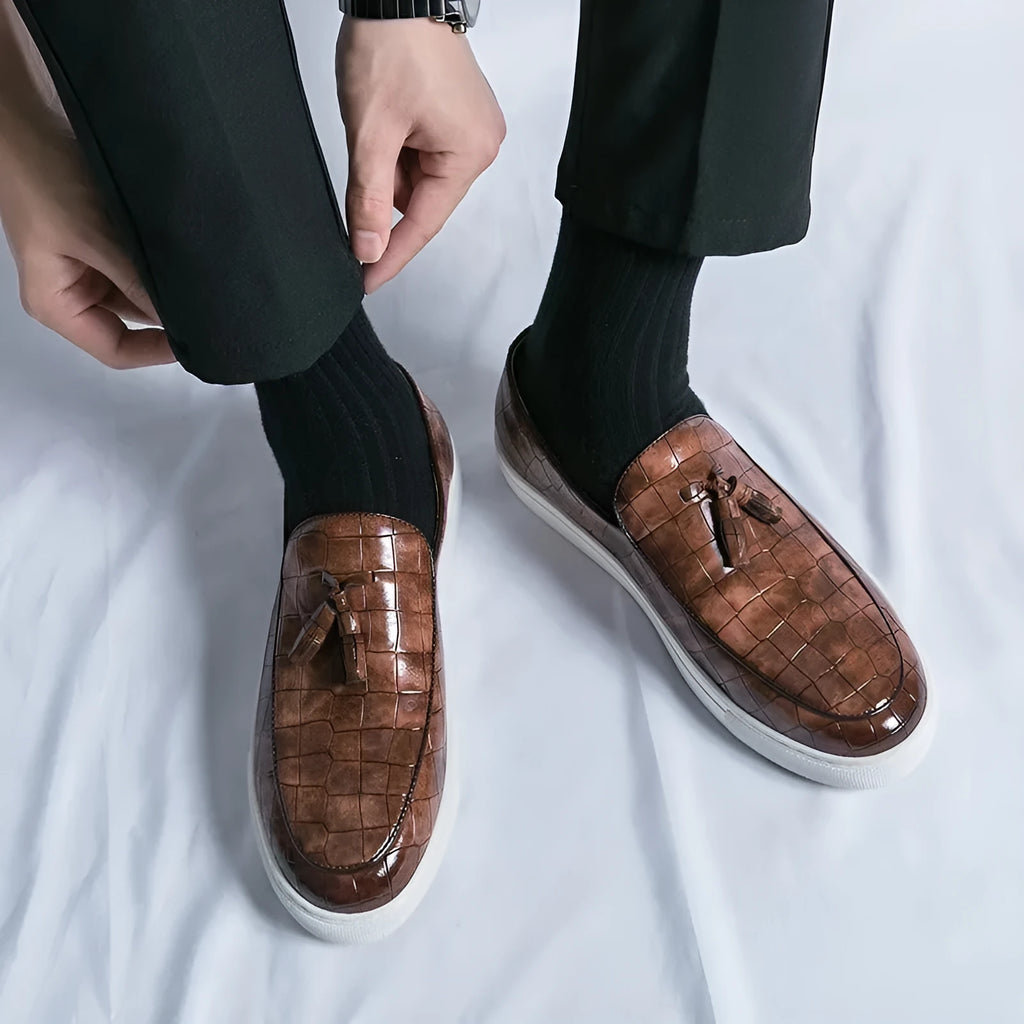 Men's black artificial leather sneaker with tassel detail on round toe, showing slip-on design.