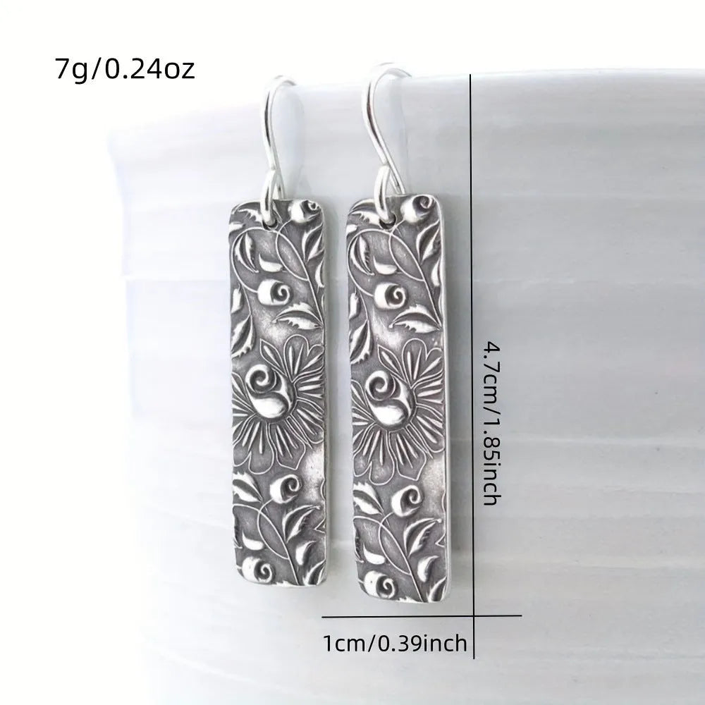 Silver geometric long strip drop earrings with carved vine pattern on a white background.