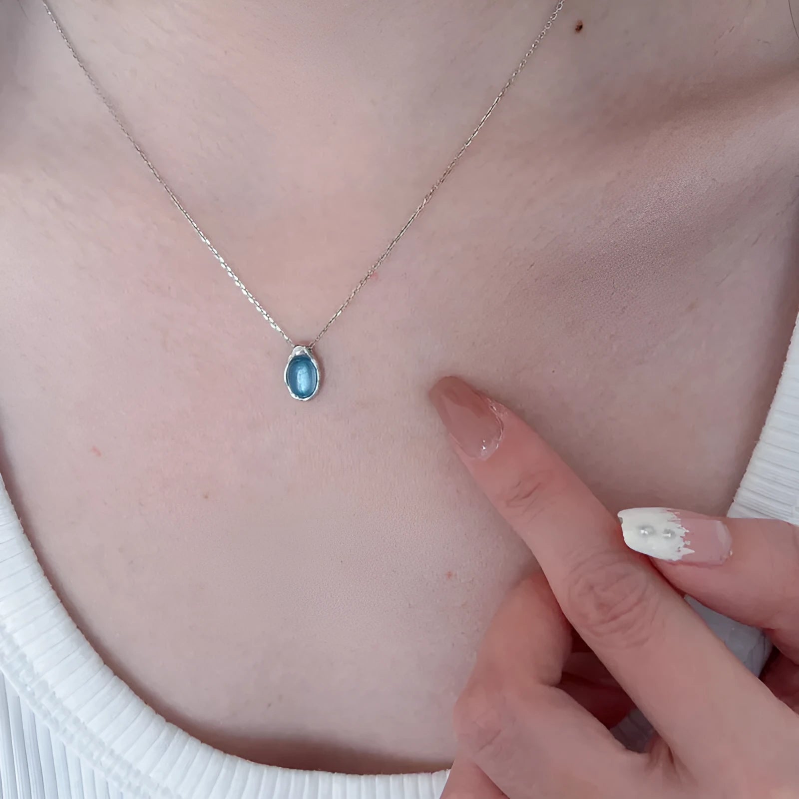 Close-up of a navy blue geometric water drop pendant on an adjustable silver-tone cross chain necklace.