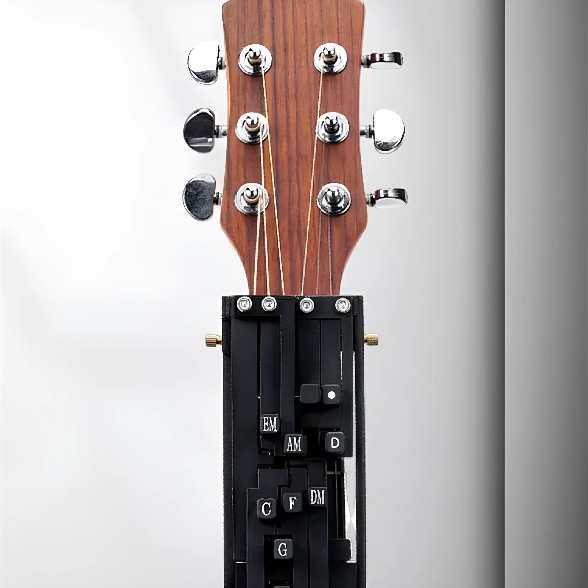 A black automatic chord maker device for guitar practice, shown next to an acoustic guitar.