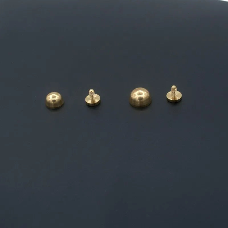 Brass decorative buckle with set of round and bucket-shaped brass foot nails on a surface.