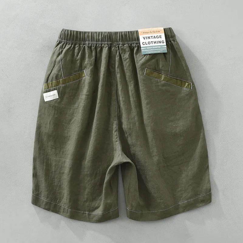 Man wearing loose fit green linen shorts with a straight leg and drawstring waist for casual summer wear.