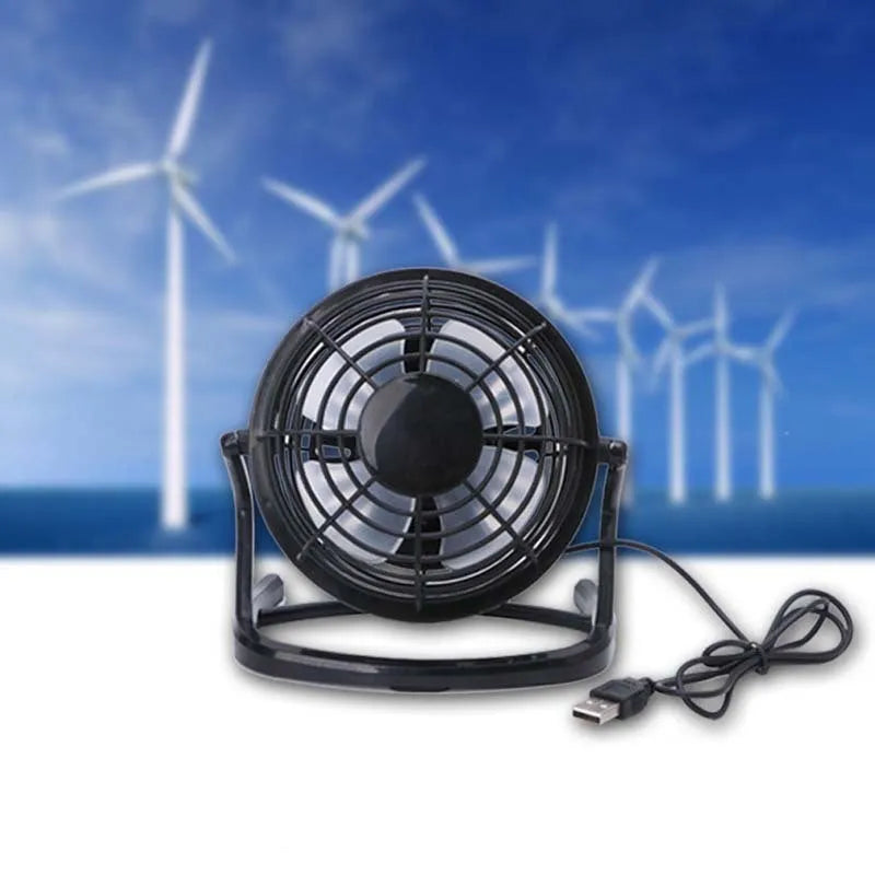 Small black and white USB desktop fan with adjustable stand on a desk next to a laptop.