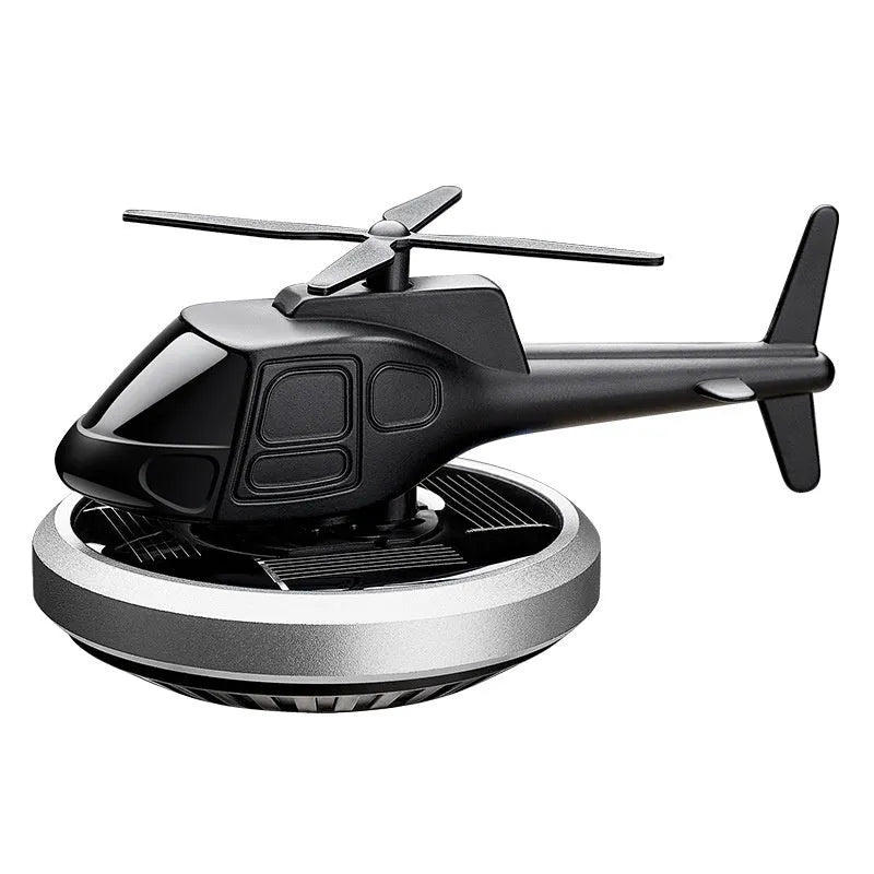 Silver metal solar-powered helicopter car air freshener with spinning blades on a dashboard.