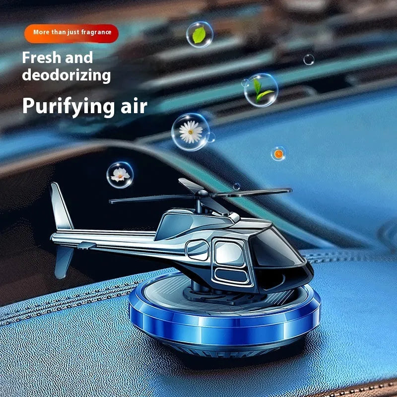 Silver metal solar-powered helicopter car air freshener with spinning blades on a dashboard.